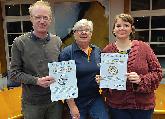Drei Mitglieder des Vereinsvorstand halten die Urkunden für das "Goldene Kettenblatt" und die "Rostige Speiche" hoch.