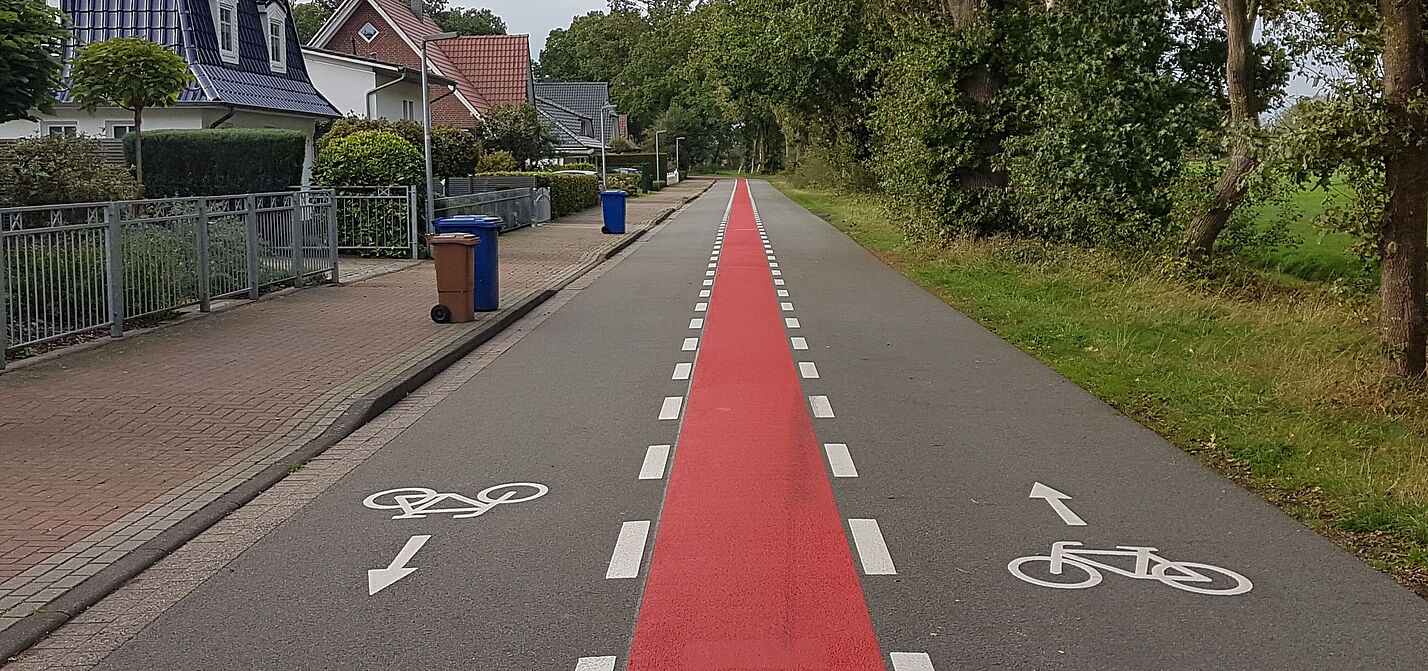 Fahrradstraße-BZw-OL-innerorts-mit-Piktogrammen Fahrradstraße innerorts, asphaltiert mit rotem Mittelstreifen und Fahrrad-Piktogrammen