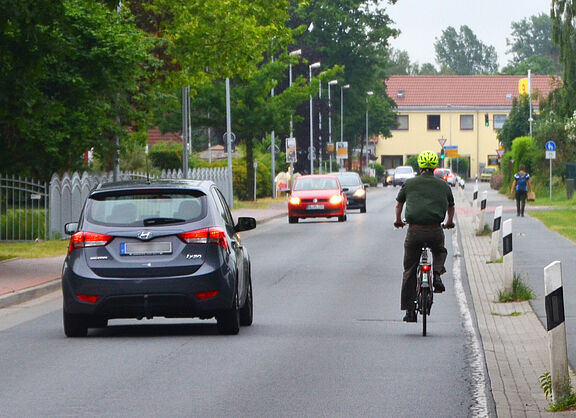 Ein Auto überholt einen Radfahrer und hält sich dabei weit entfernd von ihm