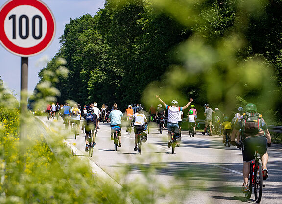 Radfahrer bei Sternfahrt neben Schild zu Geschwindigkeitsbegrenzung 100h/km