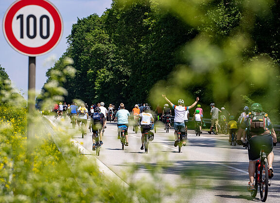 Radfahrer bei Sternfahrt neben Schild zu Geschwindigkeitsbegrenzung 100h/km